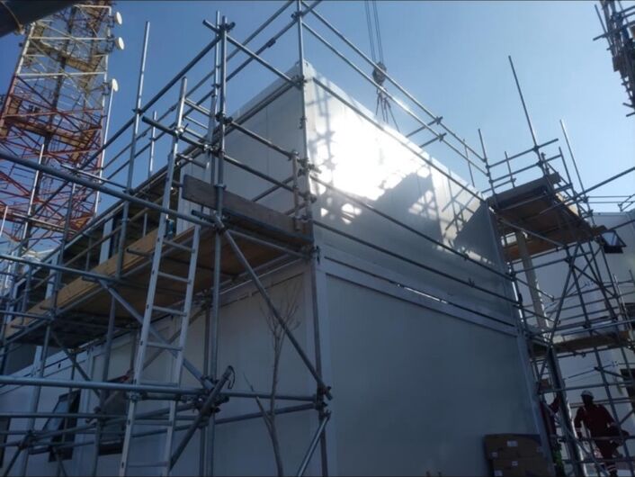 Facade panels being installed on a modular building from scaffolding