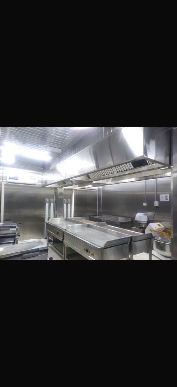 Commercial kitchen line with overhead extraction hoods and stainless-steel worktops